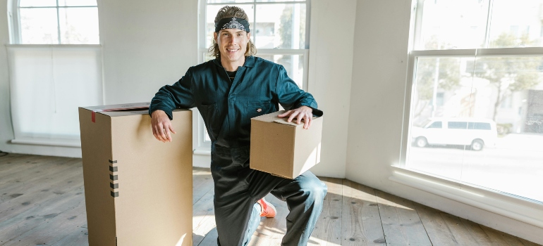 Smiling mover holding a cardboard box inside an empty home, representing trusted moving companies marble falls tx.