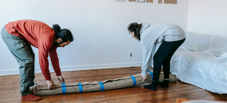 Couple rolling a rug while packing, reflecting housing changes linked to the cost of living in Austin TX.